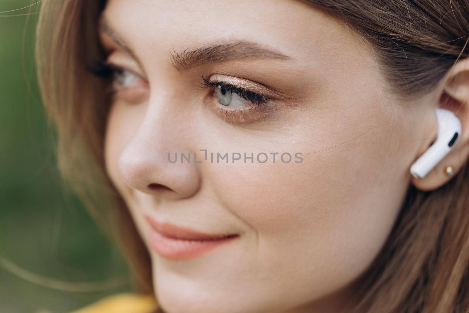 Close up face portrait of a lovely young fitness girl listening to music through wireless earphones outdoors by uflypro
