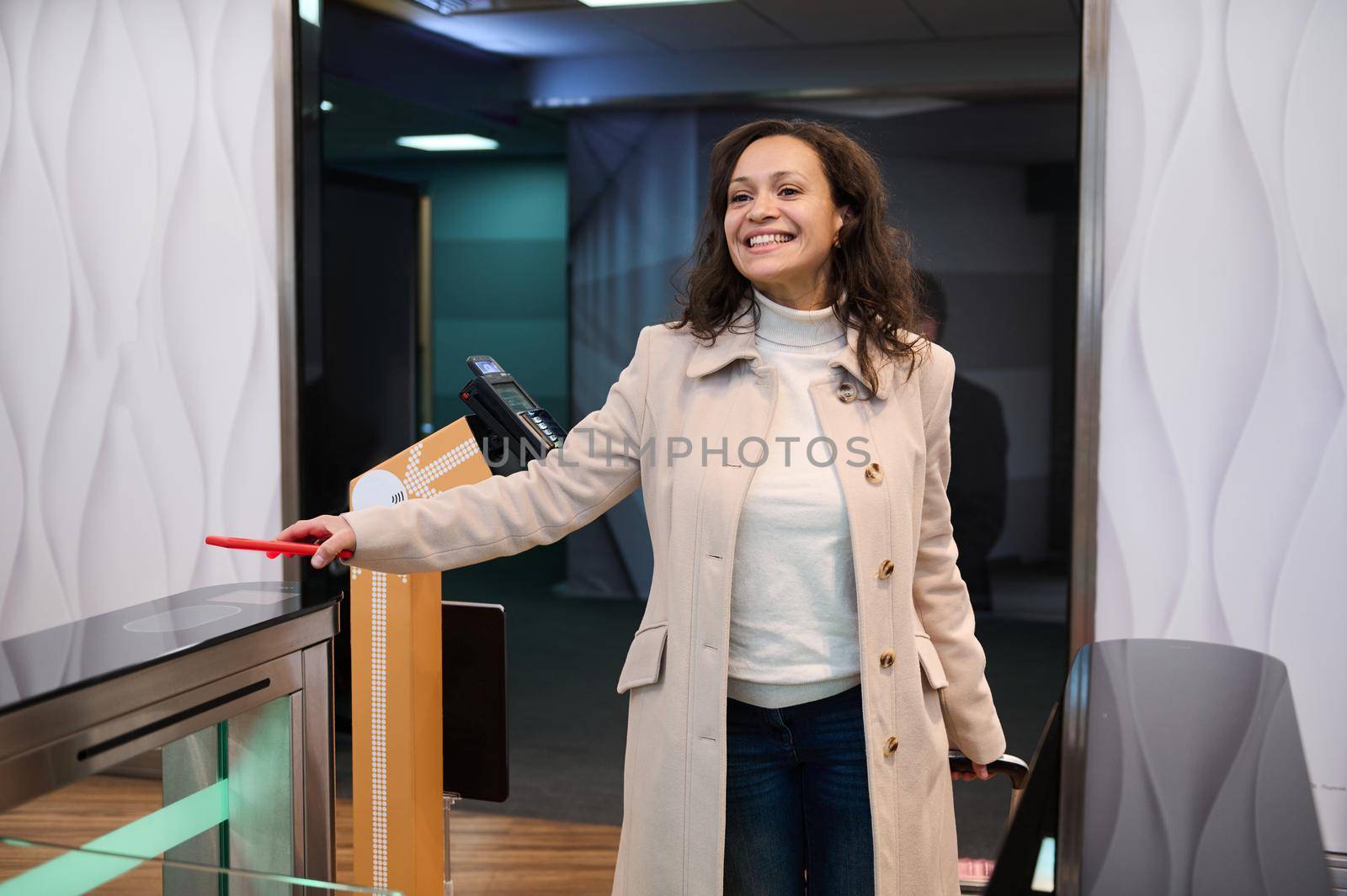 Smiling multiethnic beautiful woman, in casual wear on a business trip, scans information on her smartphone, places it over the QR code reader at the check-in counter in the airport departure terminal