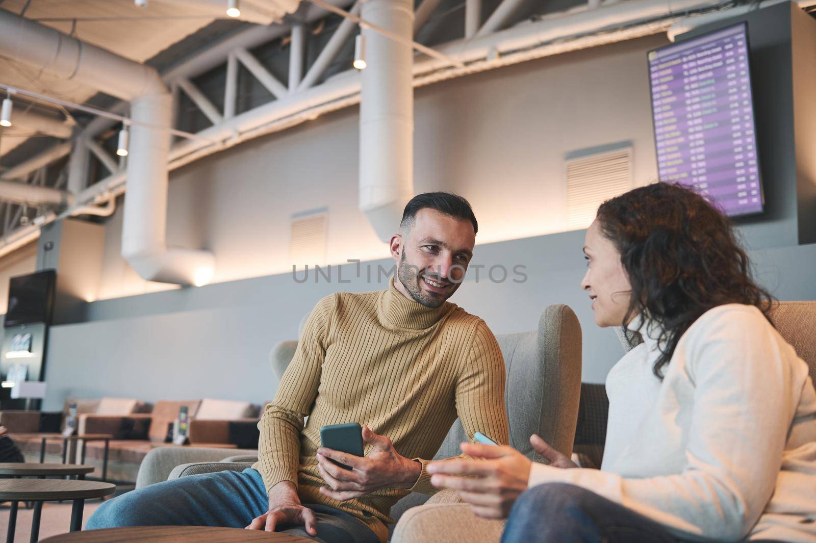 Business partners, team of colleagues, cheerful loving multiethnic couple in love, travelling together, waiting to board the flight in the international airport departure terminal