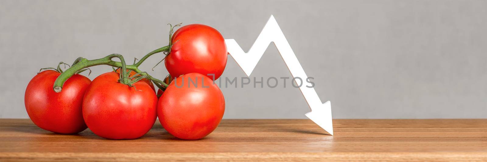 The price of tomatoes and vegetables. Bad vegetable harvest. Fresh red ripe tomatoes with twigs on the table. Graph chart points down. by SERSOL