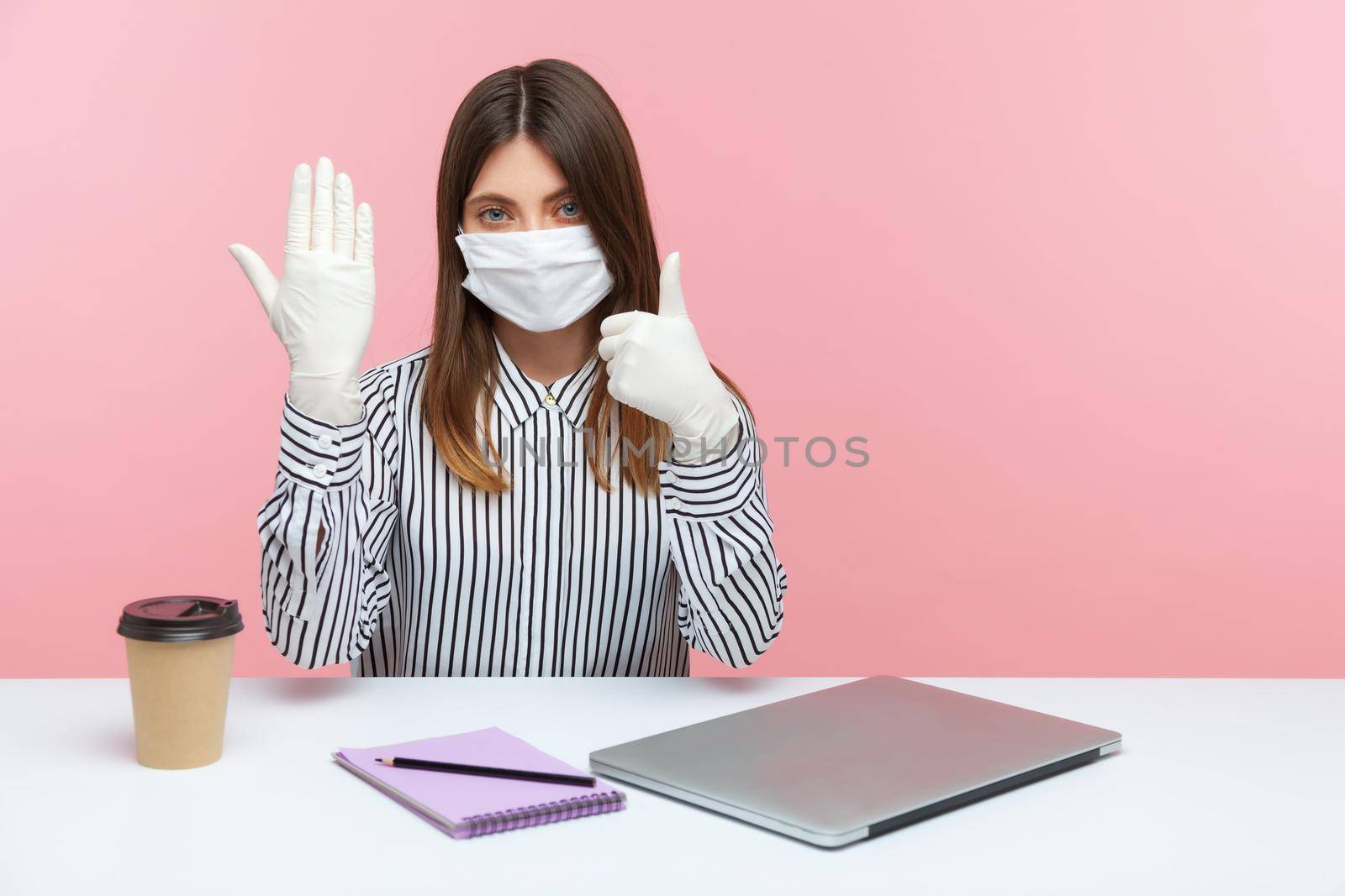 Good protection against coronavirus infection. Woman office employee sitting at workplace, feeling safe healthy with protective mask and gloves during covid-19 quarantine, showing thumbs up. indoor