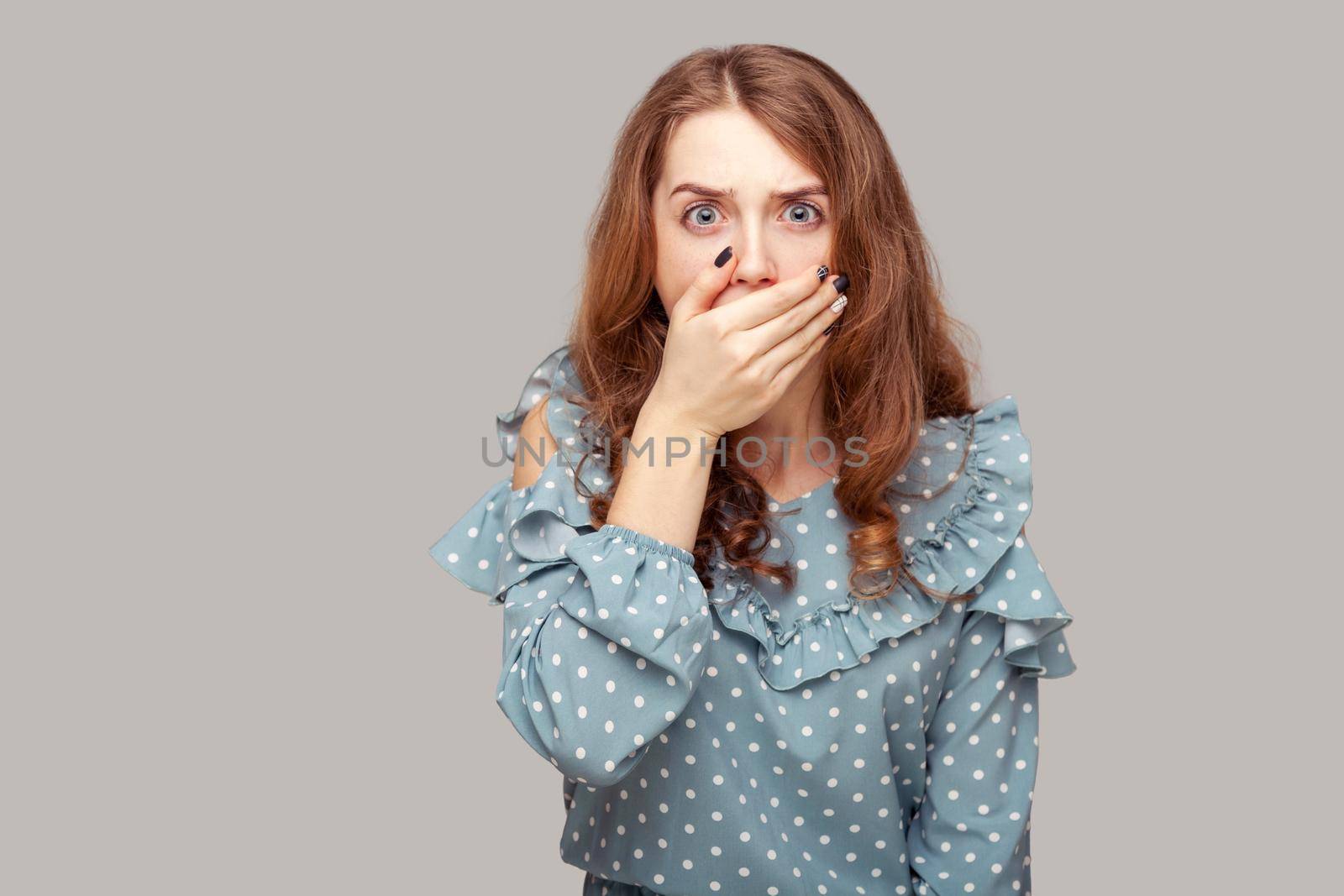 Won't say anyone. Shocked frightened girl ruffle blouse covering mouth intimidated scared to talk, looking surprised terrified, keeping terrible secret. indoor studio shot isolated on gray background