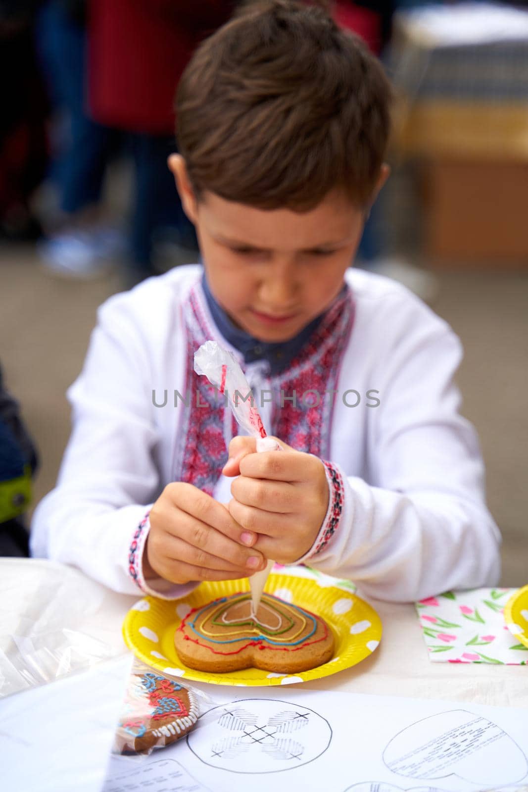 Vyshyvanka day in Ukraine. Kid painting Ukrainian flag in shape of heart on gingerbread by Try_my_best