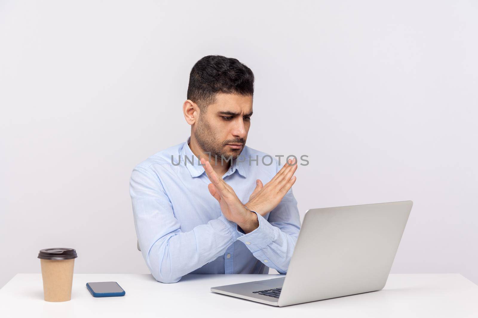 This is the end. Strict male boss sitting office workplace, crossing hands showing x sign stop gesture to laptop screen, finishing video call, warning of troubles. indoor studio shot, white background