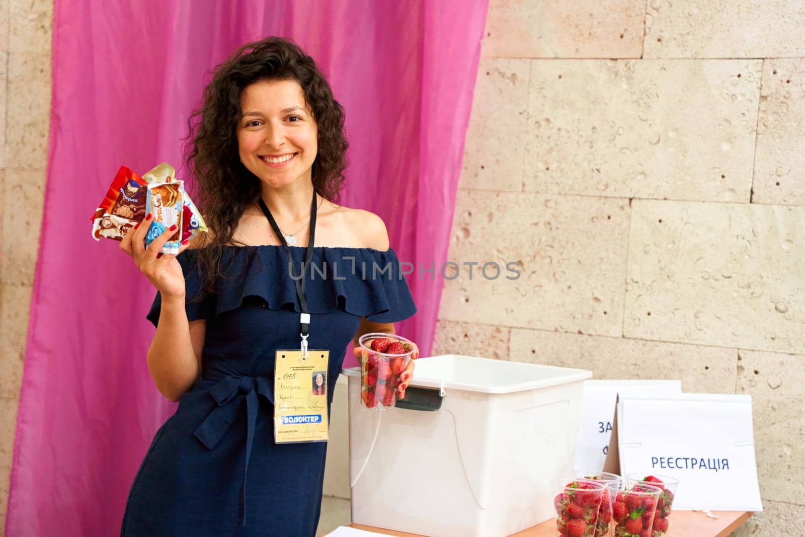 Gorgeous Ukrainian volunteer woman gives sweets and strawberry to kids. Dnipro, Ukraine - 06.10.2022