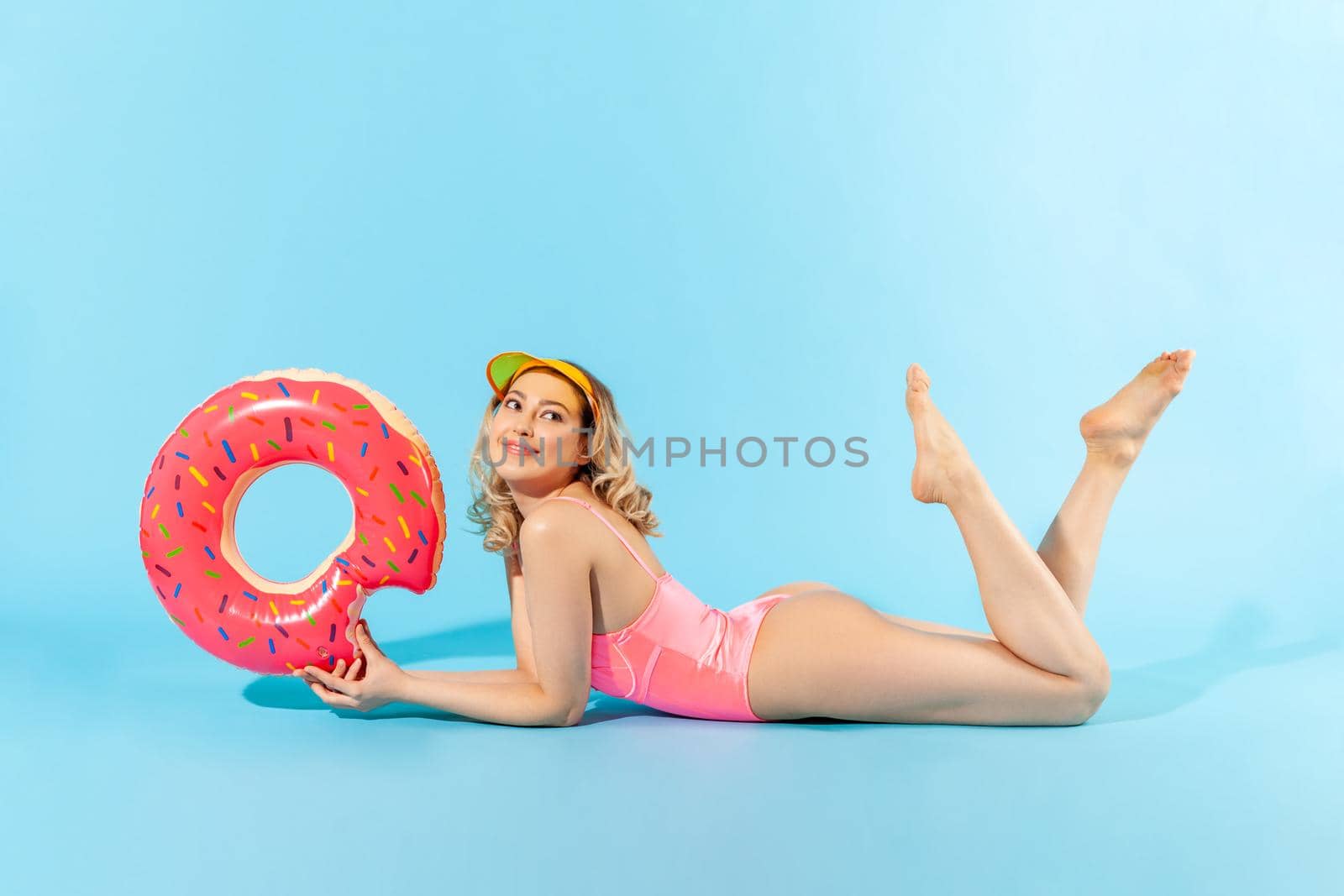 Full length attractive lovely woman in swimsuit lying sexy, holding rubber ring and dreaming with smile, sunbathing on summer beach, rest on vacation resort. studio shot isolated on blue background