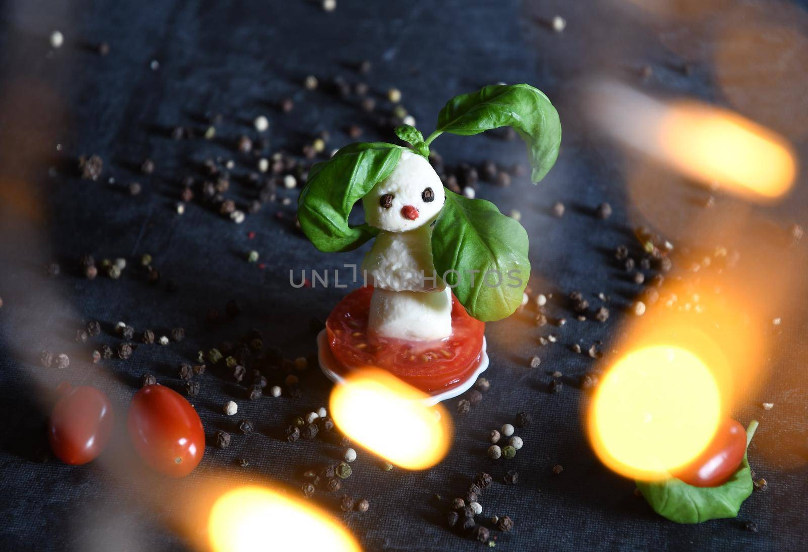 creative snowman canapes of mozzarella and tomatoes on a background of red poinsettia and a scattering of black pepper and green basil. High quality photo
