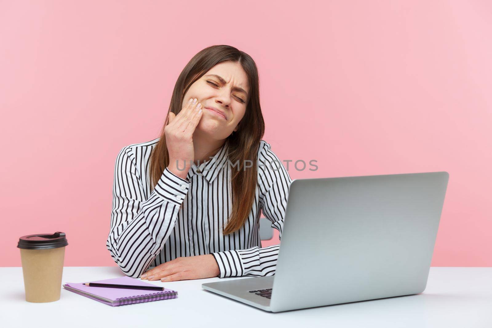 Unhappy dissatisfied woman office worker touching cheek feeling pain and discomfort in oral cavity, toothache and gums inflammation. Indoor studio shot isolated on pink background