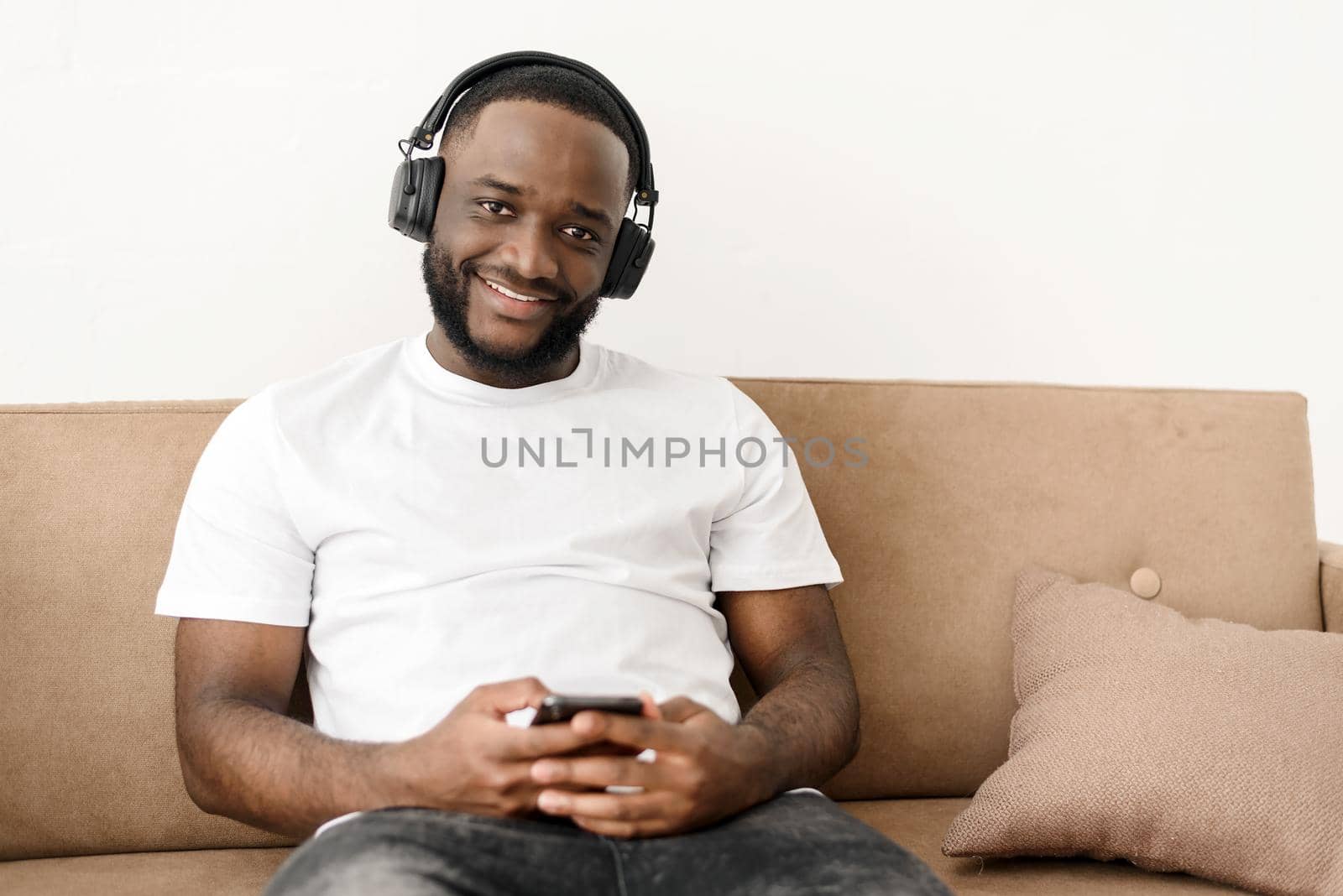 Portrait of an african american young guy enjoying listening to good music at home, sitting on the sofa, looking at camera.