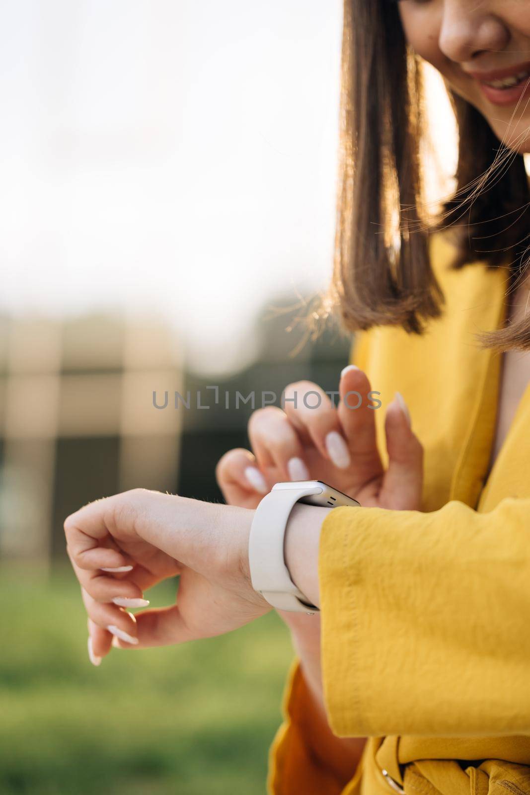 Appealing young elegant woman touching a smartwatch. Caucasian woman use her wearable smart watch and smiling. Smart watch. Smart watch on a woman's hand outdoor.