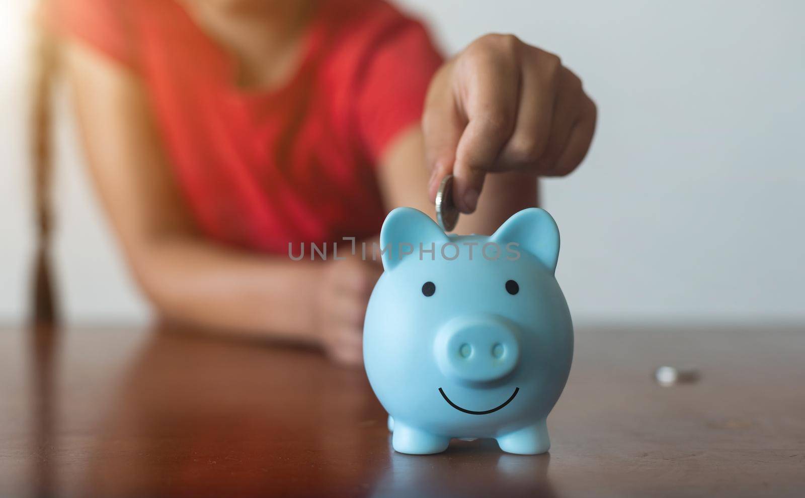 Smiling little girl posing with a piggy bank in her hands, standing against a blue background in a studio with free space. Family savings.