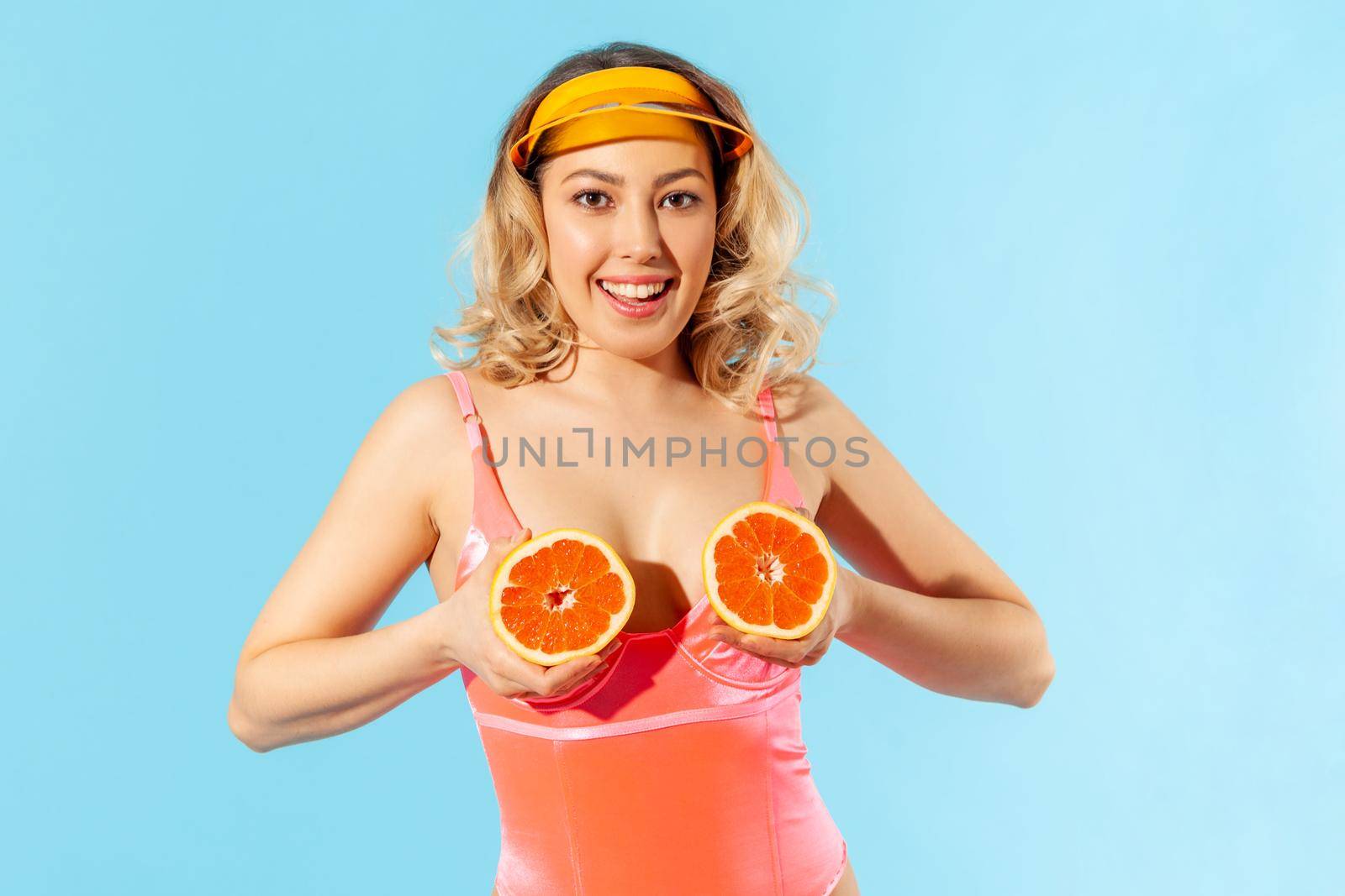 Portrait of cheerful pretty woman in swimsuit holding fresh cut orange and looking at camera with toothy smile. Concept of female beauty, natural cosmetic antioxidant, healthy nutrition isolated