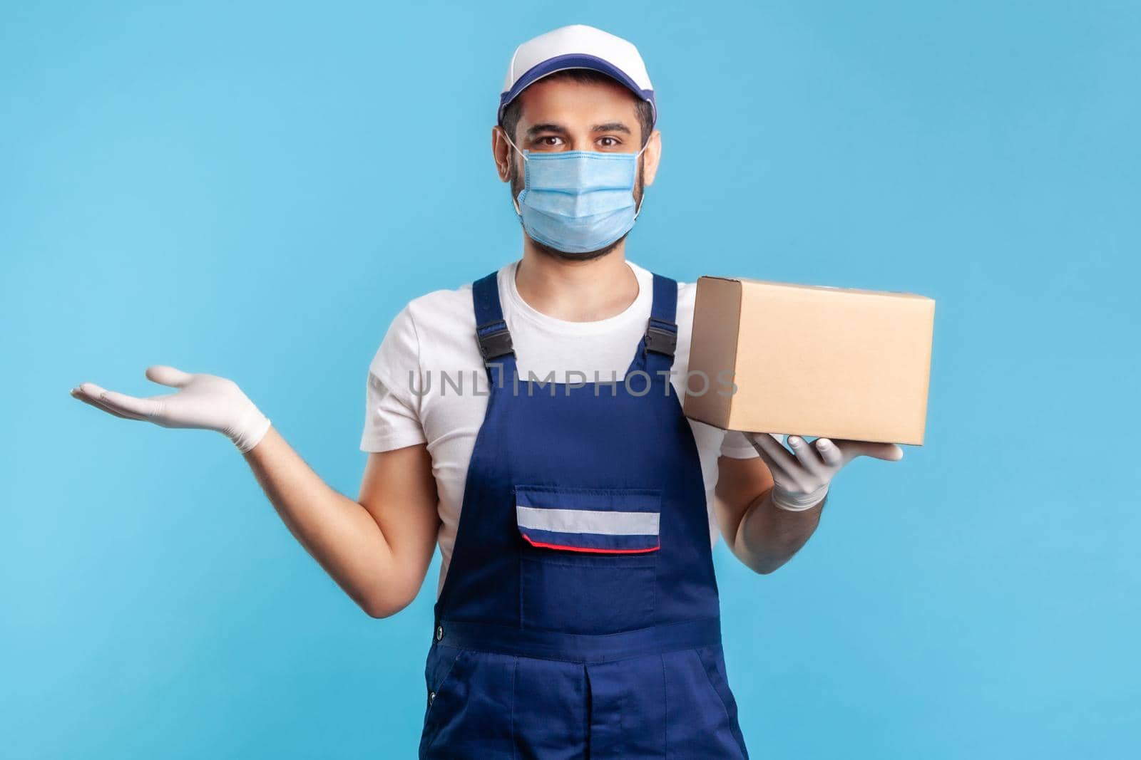 worker in uniform and mask carrying cardboard box and raising other hand to hold empty space, advertising area for commercial image. Concept of cargo transportation, delivery service, express shipping