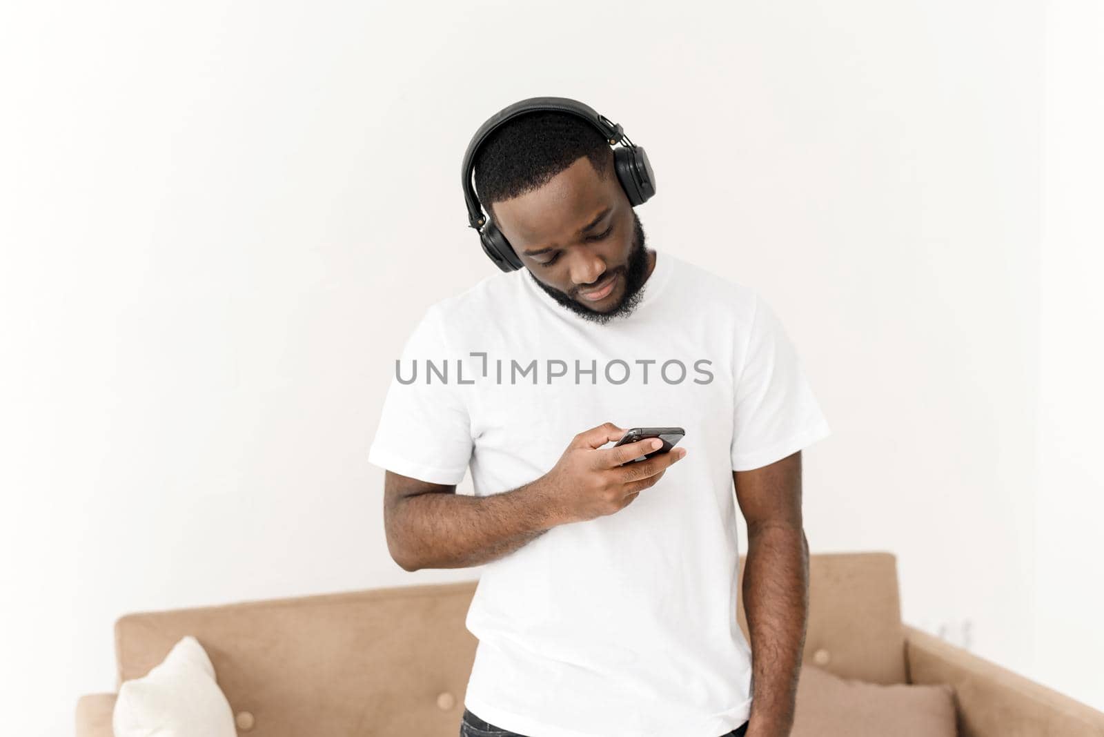 Portrait of an african american young guy enjoying listening to good music at home, looking at the smartphone screen