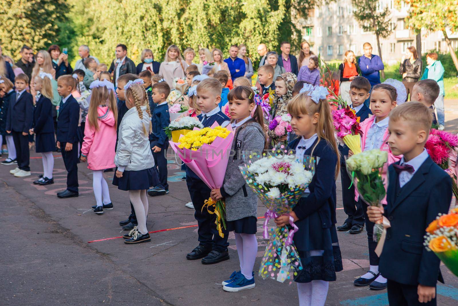 NOVOKUZNETSK, KEMEROVO REGION, RUSSIA - SEP, 1, 2021: Meeting with the first-grade pupils and teacher at schoolyard. The day of knowledge in Russia.