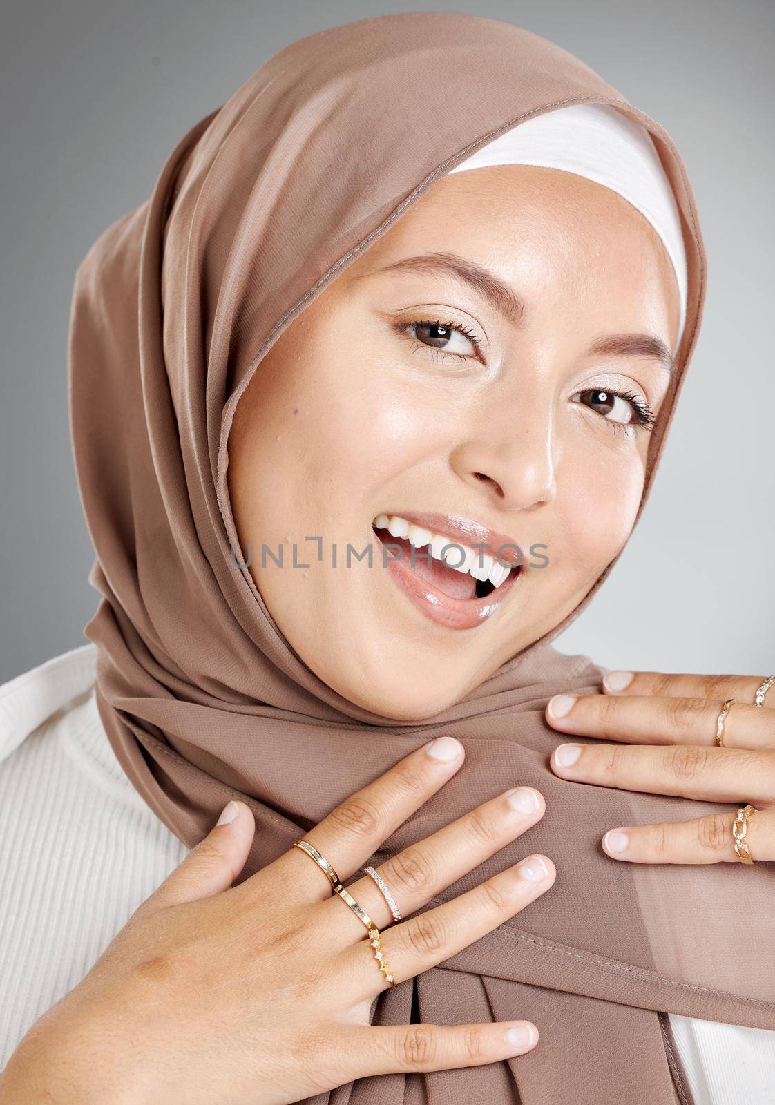 Studio portrait of beautiful and modest muslim woman isolated against a grey background. Young woman wearing a hijab or headscarf showing traditional arab modesty while smiling and looking at camera.