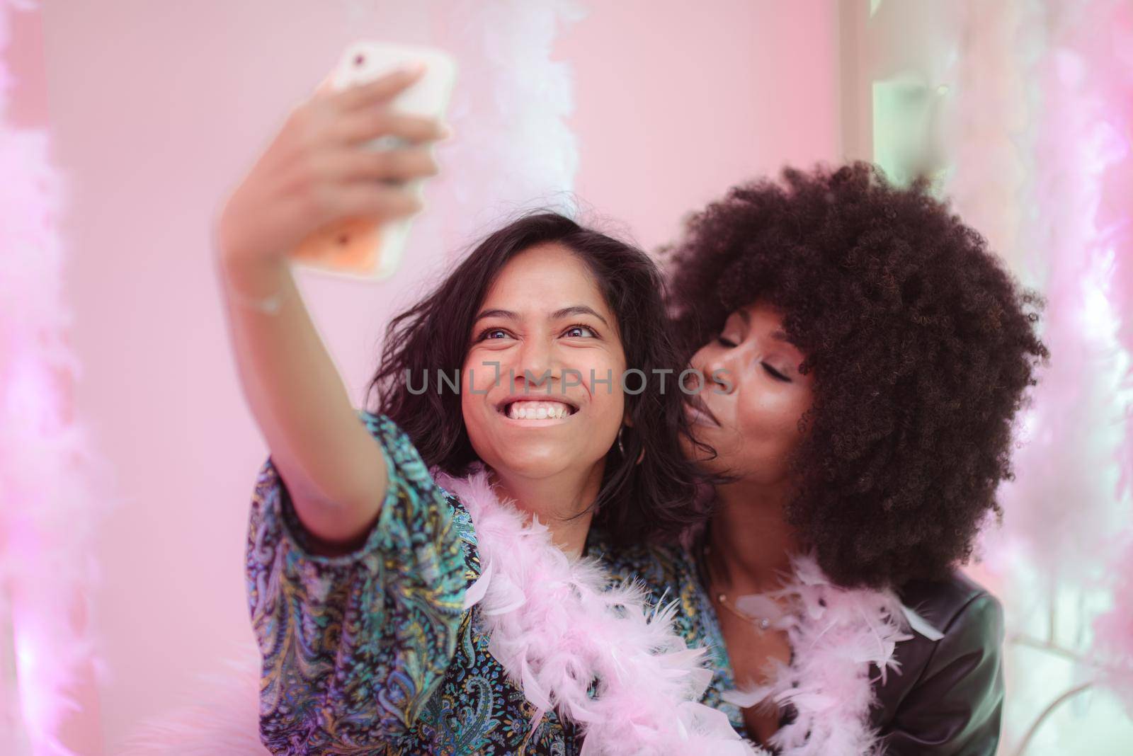 Couple of young south asian woman and african amercian woman having fun taking selfies in a bar.