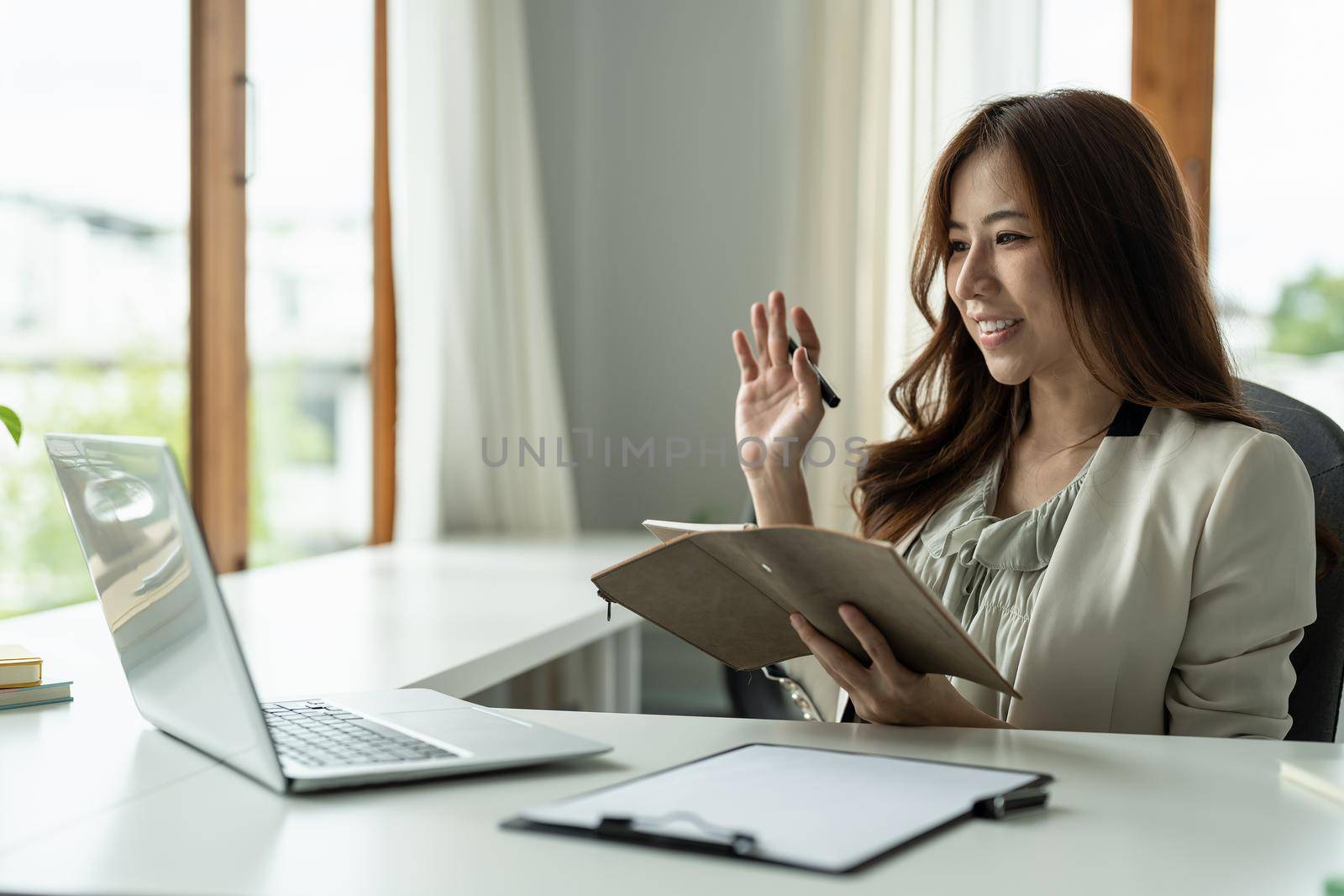 Young asian woman having conference video call using laptop talking to coworker online audience sitting at office desk in evening. Consultation, webinar, tutoring on internet, telecommuting.