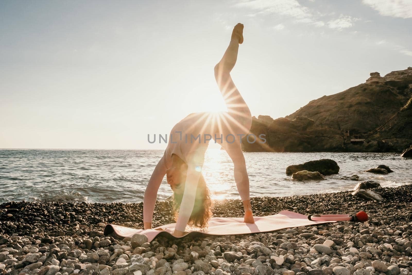 Young woman with black hair, fitness instructor in pink sports leggings and tops, doing pilates on yoga mat with magic pilates ring by the sea on the beach. Female fitness daily yoga concept