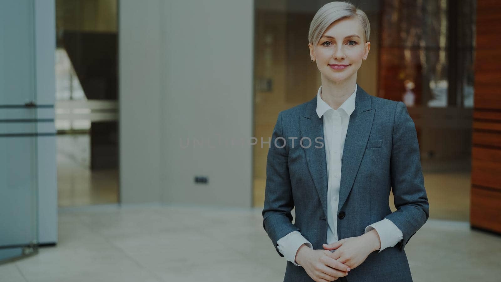 Portrait of successful blonde businesswoman smiling and looking into camera in modern office indoors