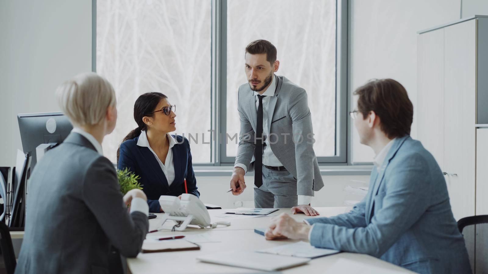 Businesswoman discussing reports with male and female colleagues sitting at the table in modern office indoors