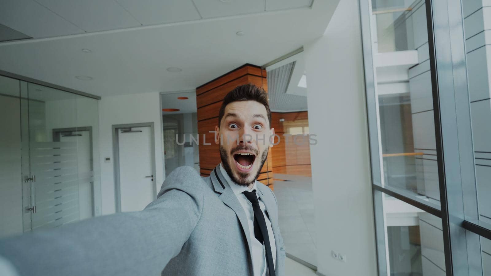 POV of young businessman in suit having online video chat using smartphone camera and talking to his colleagues in modern office indoors
