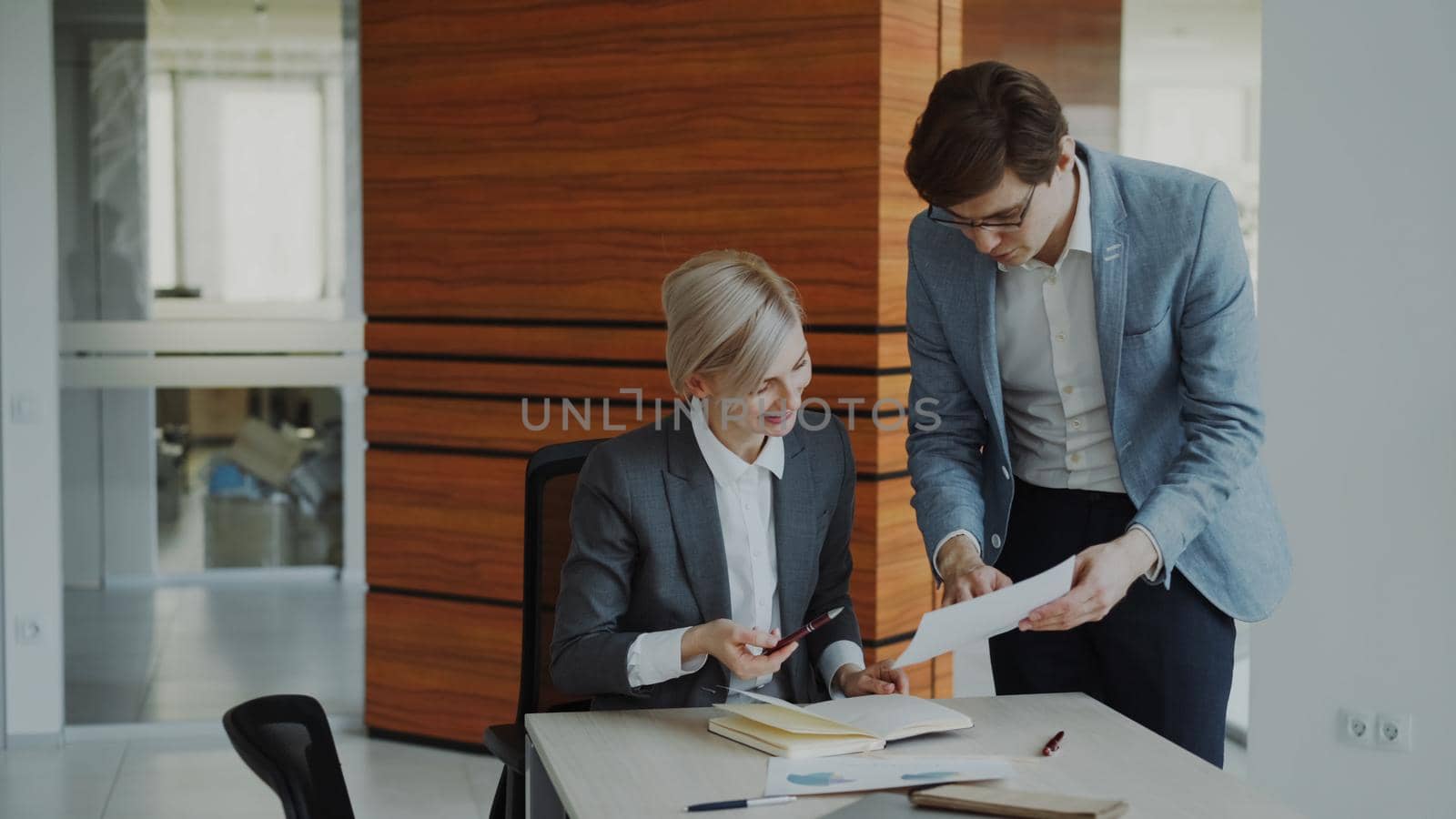 Two business colleagues discussing reports in modern office indoors. Businesswoman sitting at the table talking his male partner