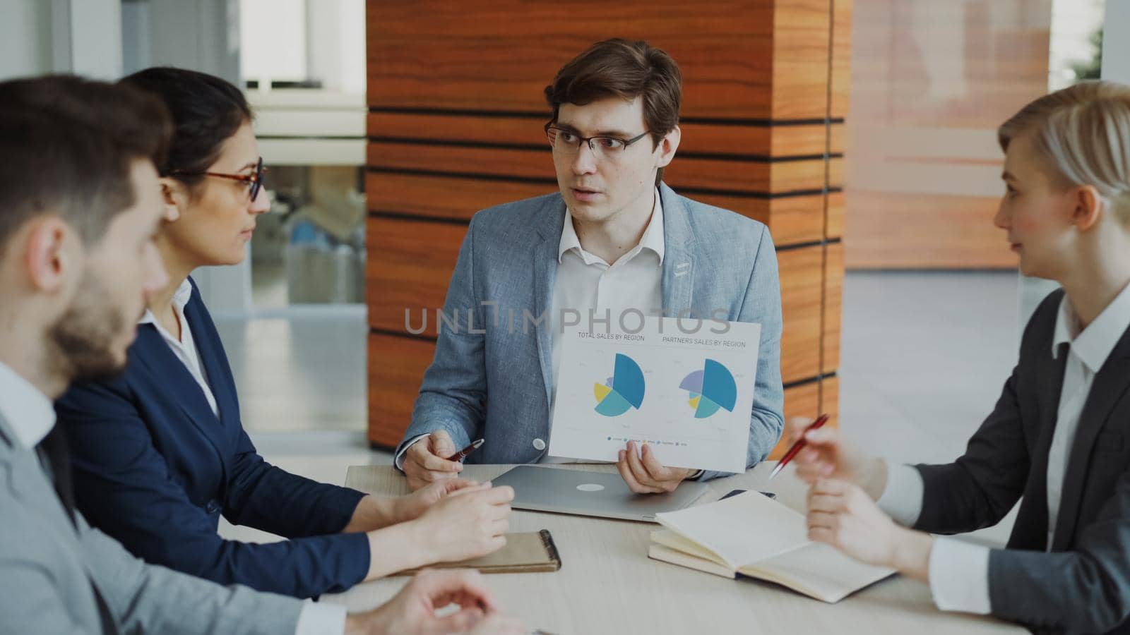 Angry businessman disappointed with company financial reports and scolding employees sitting at the table in meeting room indoors