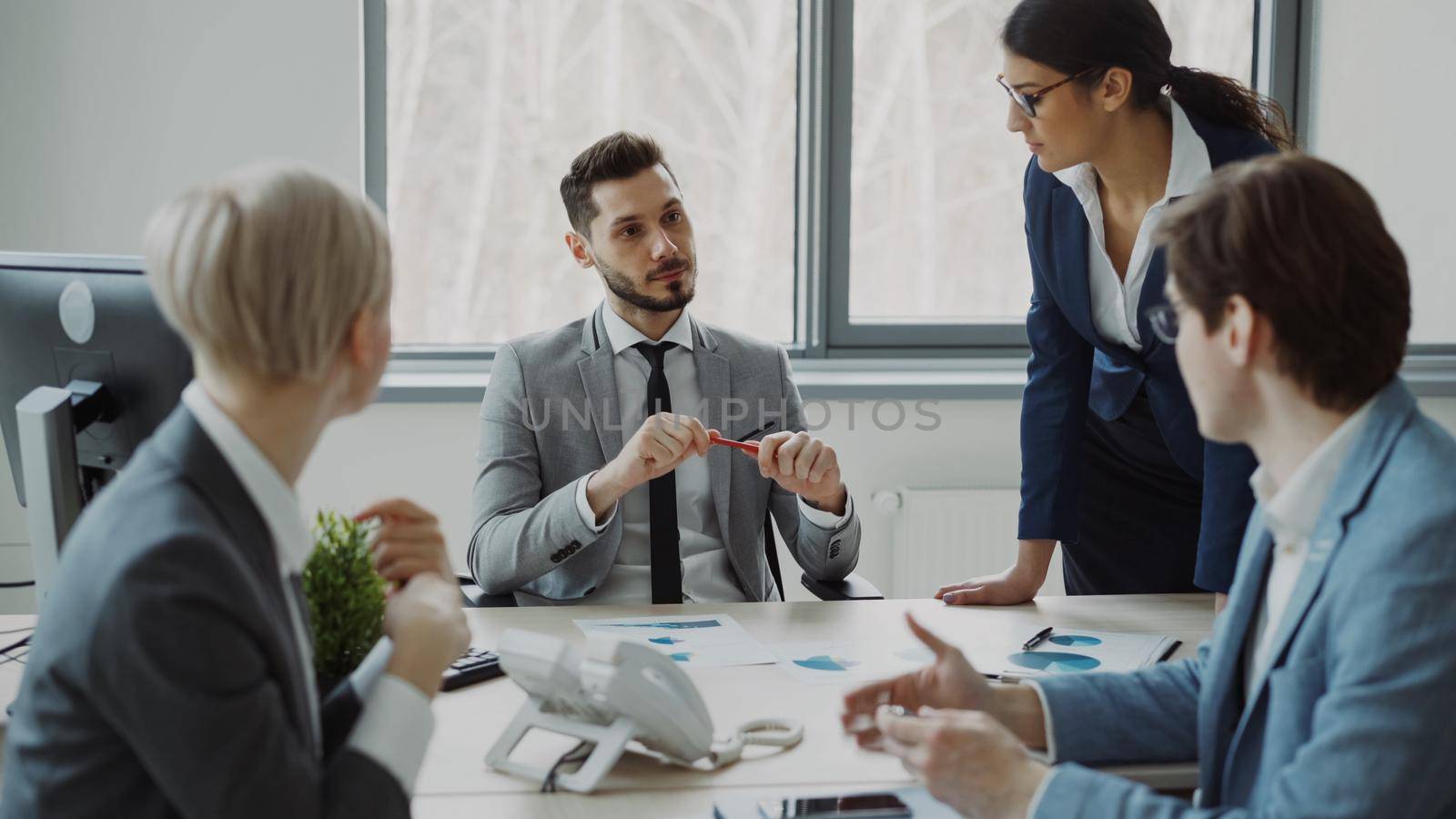 Young businessman talking with male and female colleagues sitting at the table in modern office indoors