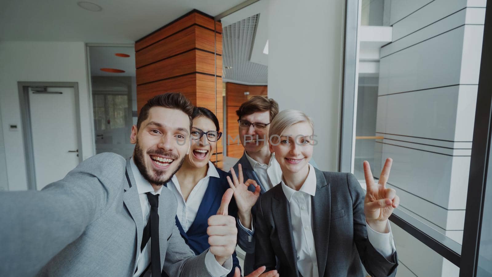 POV of Happy business team taking selfie portrait on smartphone camera and posing for group photo during meeting in modern office by silverkblack