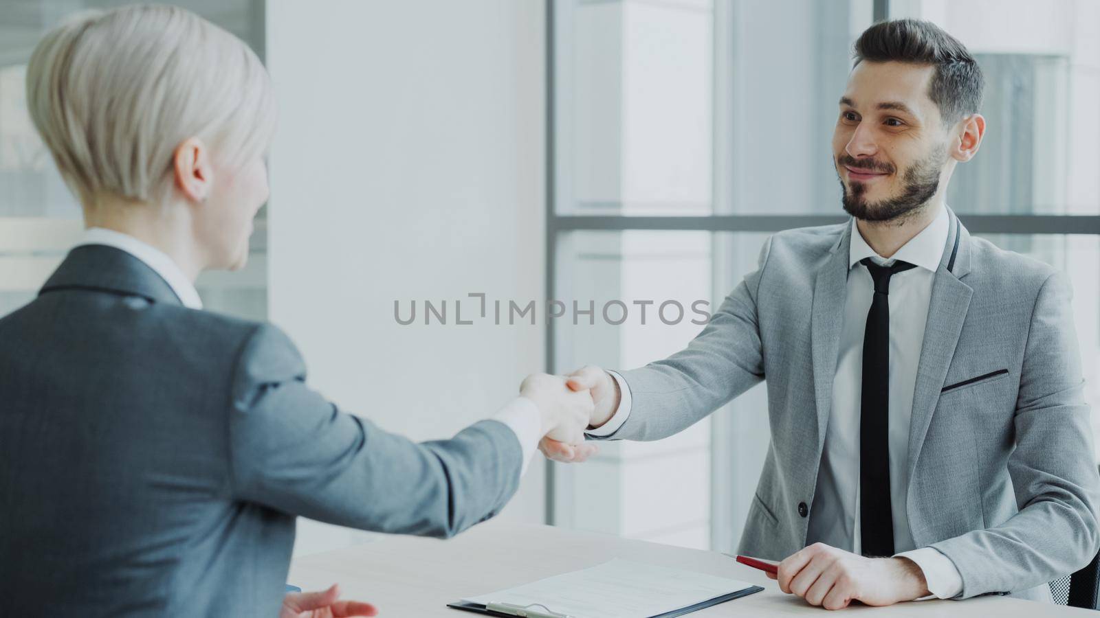 HR male manager shaking hand to female candidate after having job interview in modern office by silverkblack