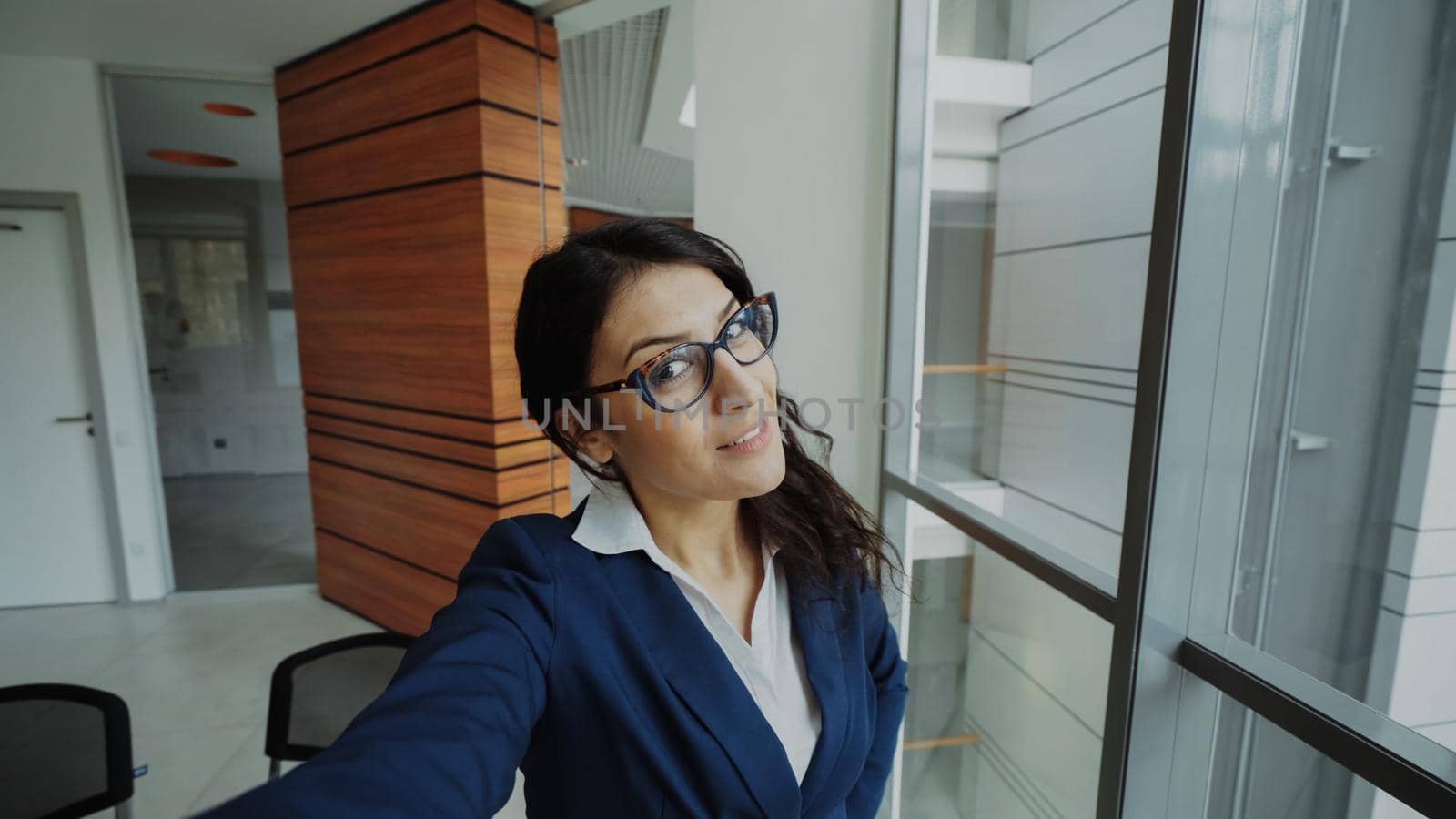 POV of young businesswoman in suit taking a selfie photo holding smartphone and have fun in modern office indoors
