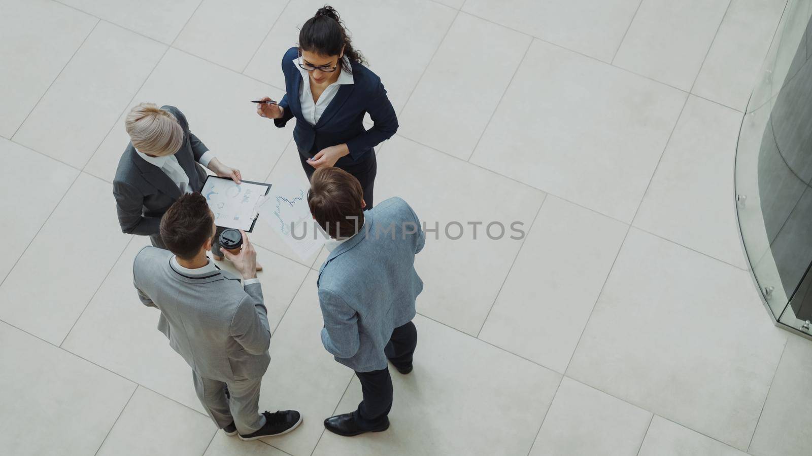 Top view of group of business people in suits discussing financial graphs in lobby of business center indoors by silverkblack