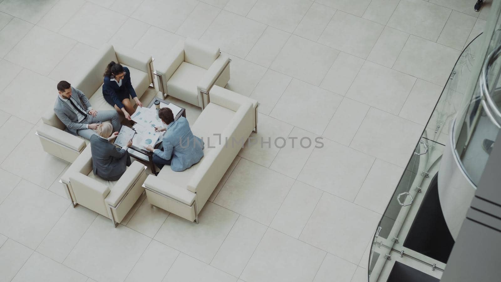 Top view of group of business people colleagues discussing financial charts sitting on couchs in lobby at modern business center indoors