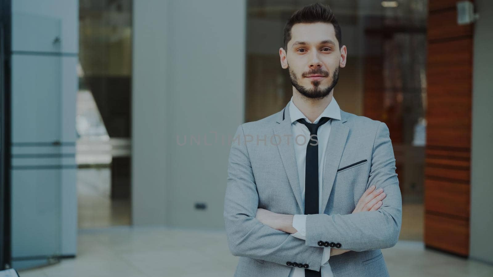 Portrait of successful young smiling businessman looking into camera in modern office by silverkblack
