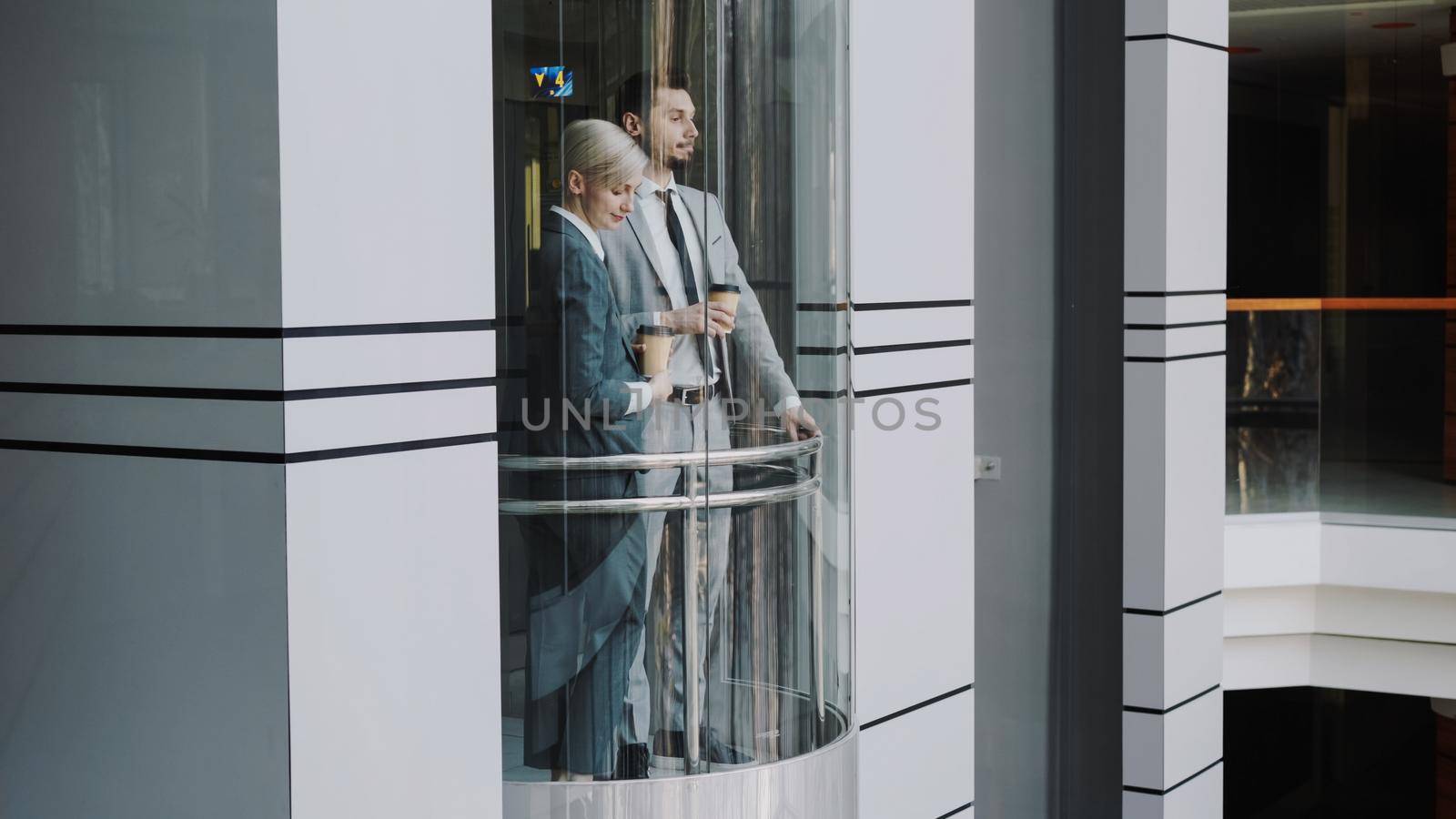 businesswoman and businessman colleagues talking in moving elevator in modern business center by silverkblack