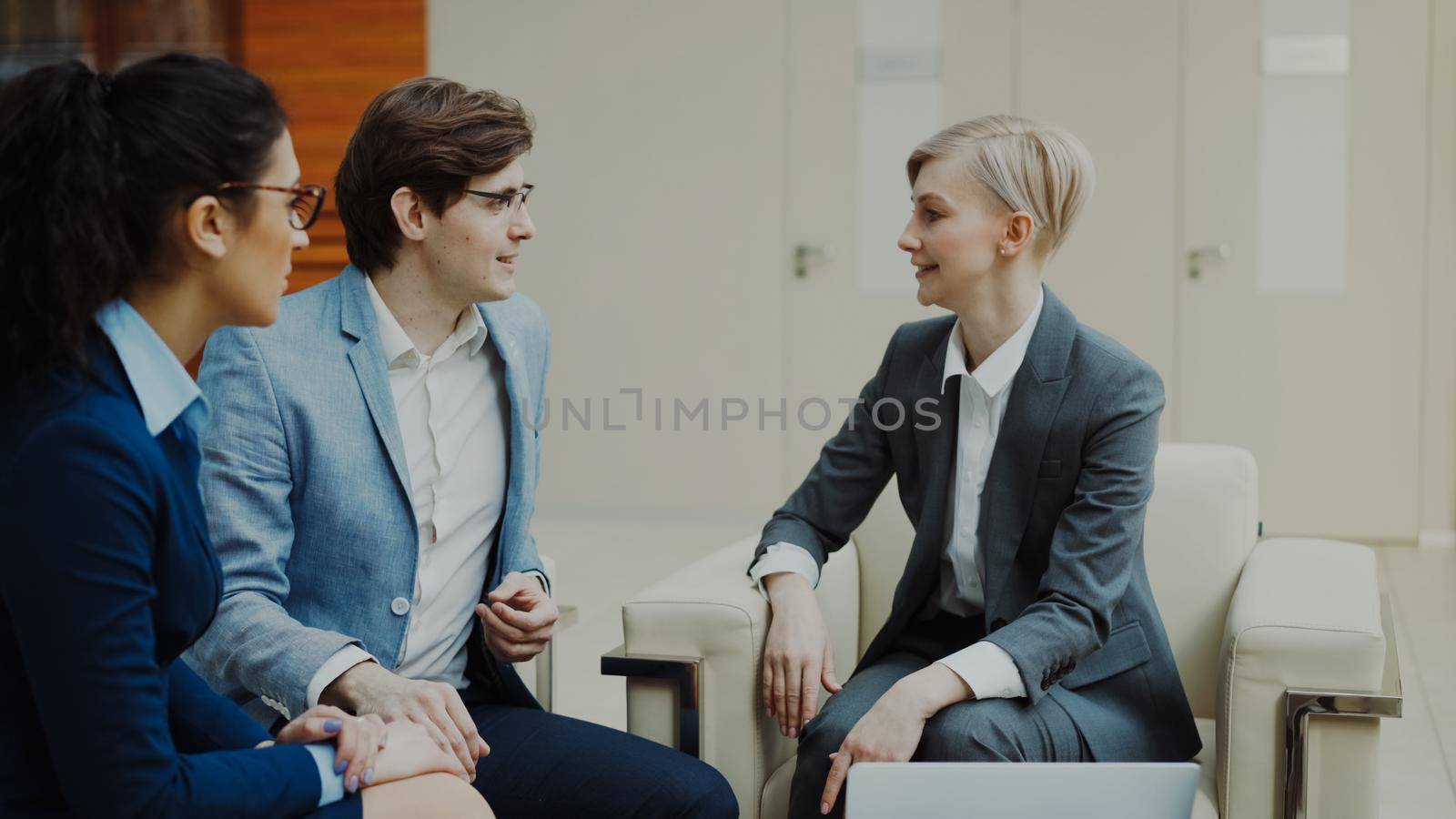 Businesswoman talking and duscussing future deal with business partners sitting on couch in modern office center by silverkblack