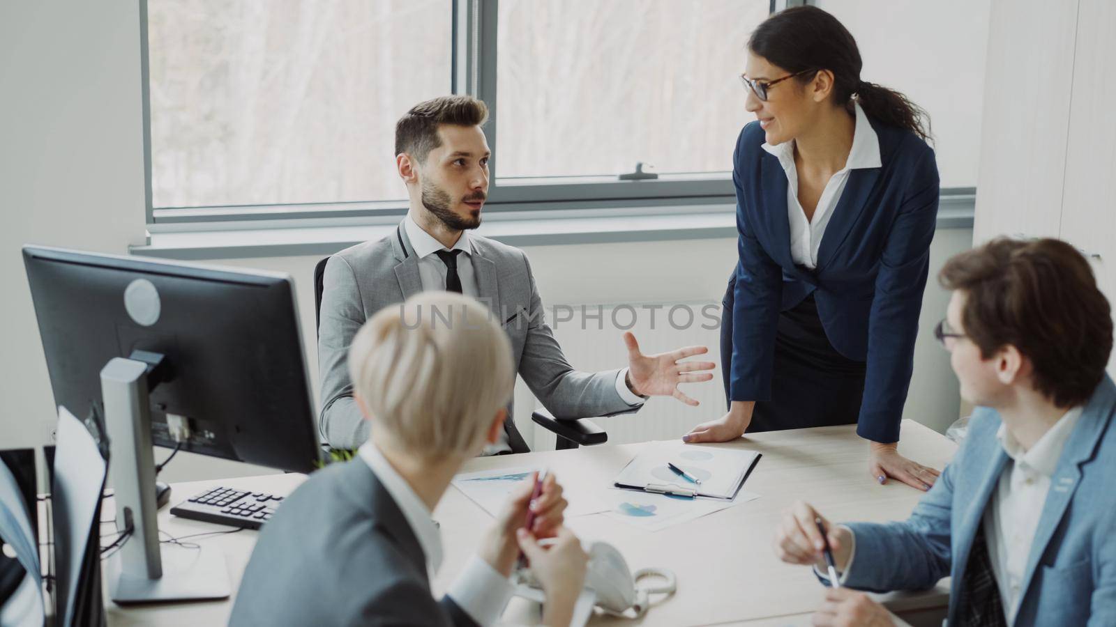 Young businessman talking with male and female colleagues sitting at the table in modern office by silverkblack