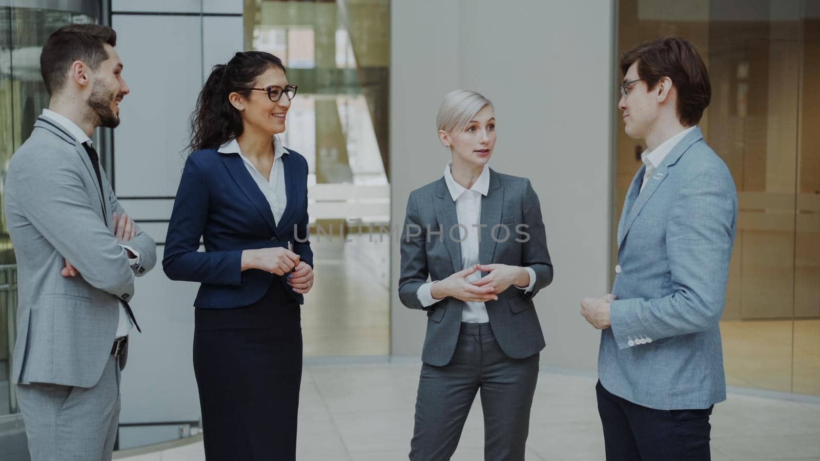 Businesswoman talking to her colleagues while standing in office lobby. Group of business people discussing future deal by silverkblack