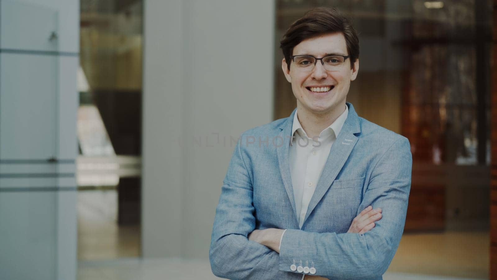 Portrait of successful smiling businessman in glasses looking into camera in modern office by silverkblack