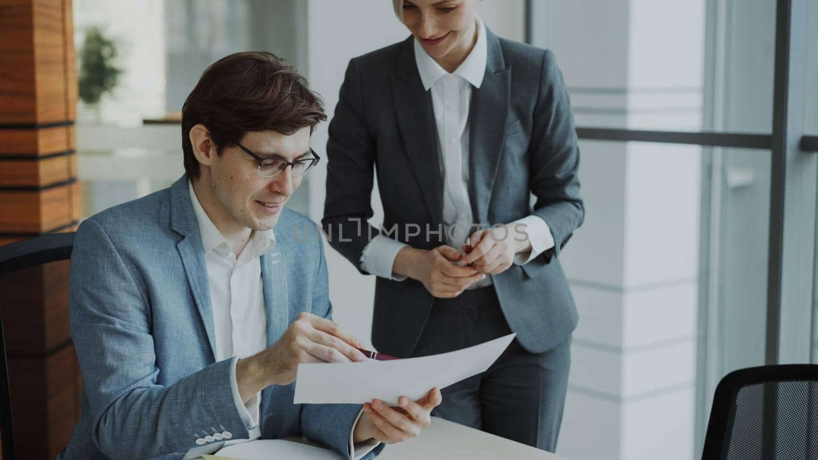 Two business colleagues discussing reports in modern office. Businessman sitting at the table talking his female partner by silverkblack