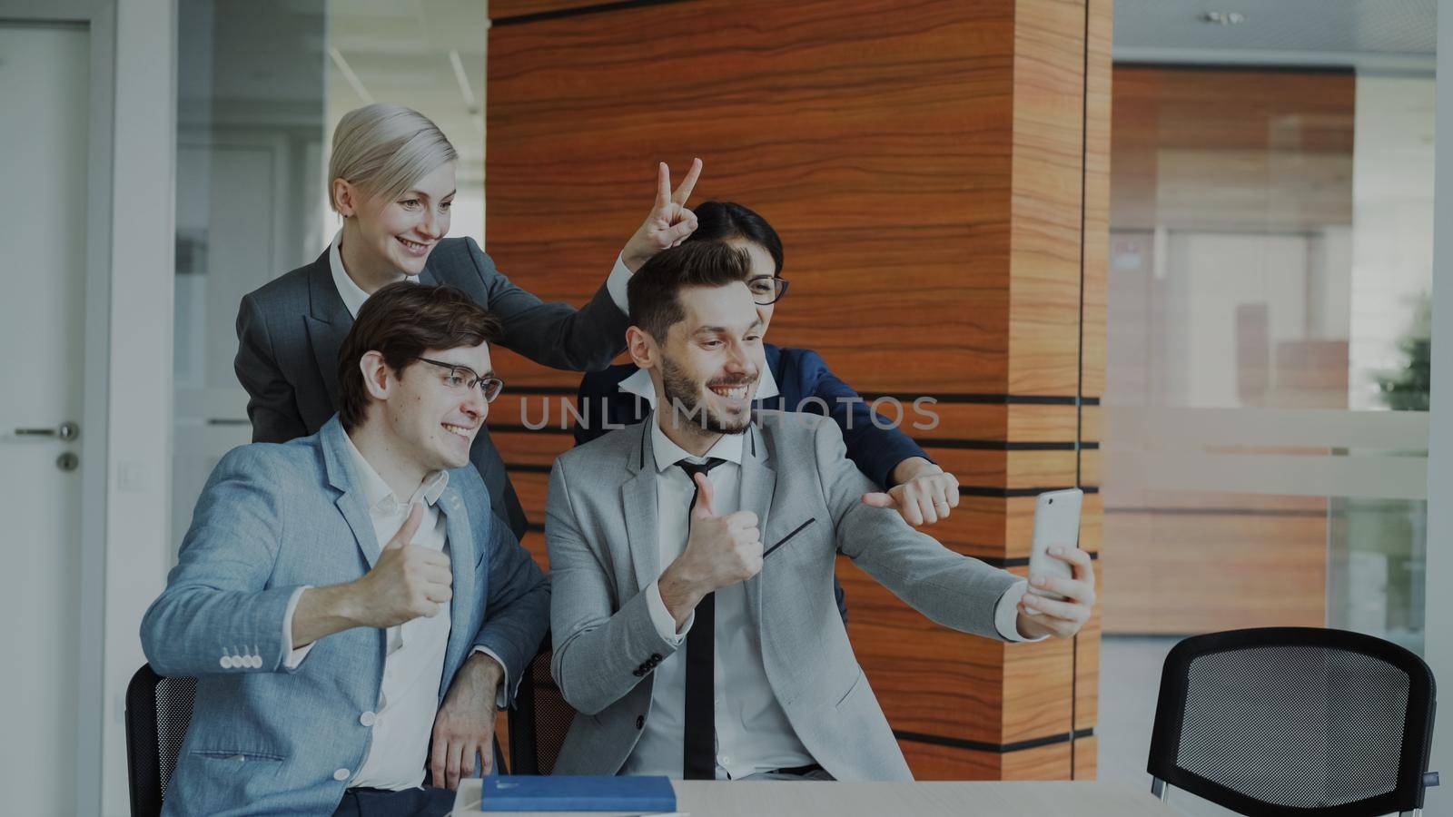 Happy business team taking selfie portrait on smartphone camera and posing for group photo during meeting in modern office indoors