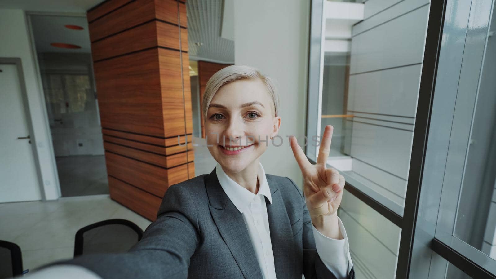 POV of young businesswoman in suit taking a selfie photo holding smartphone and have fun in modern office indoors