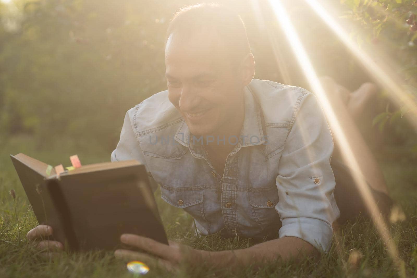 Young man lying in the grass, relaxing and reading a book.