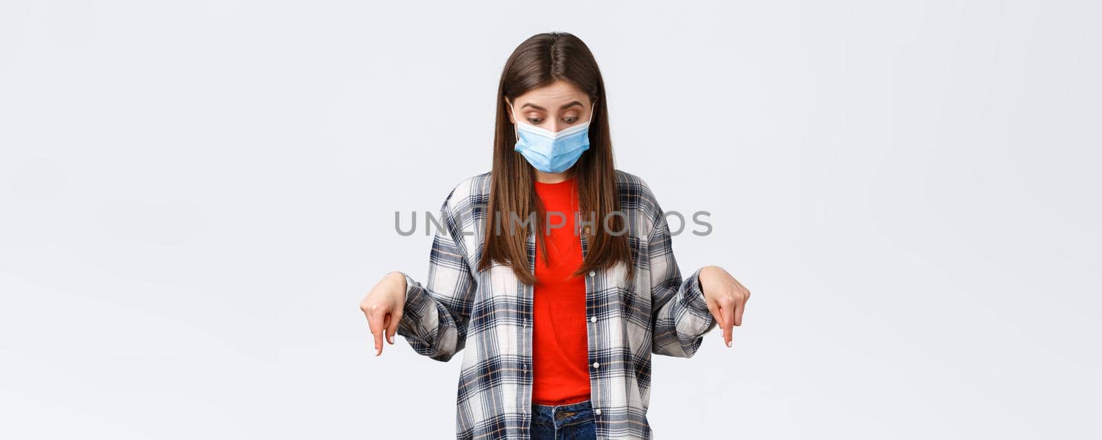 Coronavirus outbreak, leisure on quarantine, social distancing and emotions concept. Intrigued cute girl in medical mask. Woman wearing PPE from virus infection, looking pointing down by Benzoix