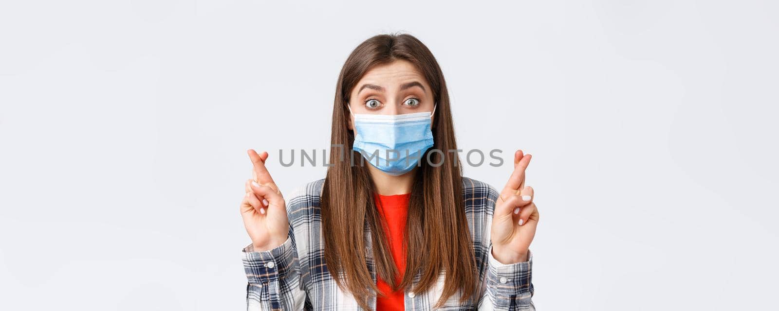 Coronavirus outbreak, leisure on quarantine, social distancing and emotions concept. Hopeful cute girl in medical mask anticipating good news, believe dream come true, cross fingers as making wish.
