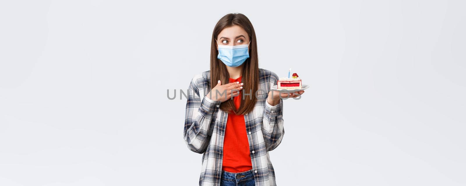 Coronavirus outbreak, lifestyle during social distancing and holidays celebration concept. Dreamy happy young girl in medical mask celebrating birthday, hold b-day cake, think what wish.