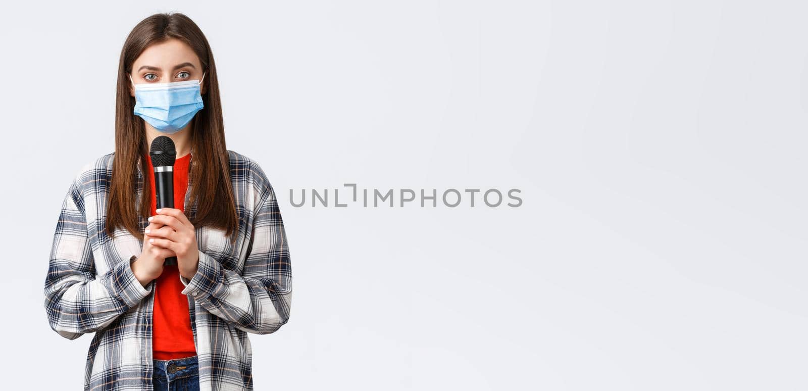 Coronavirus outbreak, leisure on quarantine, social distancing and emotions concept. Girl in medical mask performing song or stand-up, holding microphone want be heard, white background by Benzoix