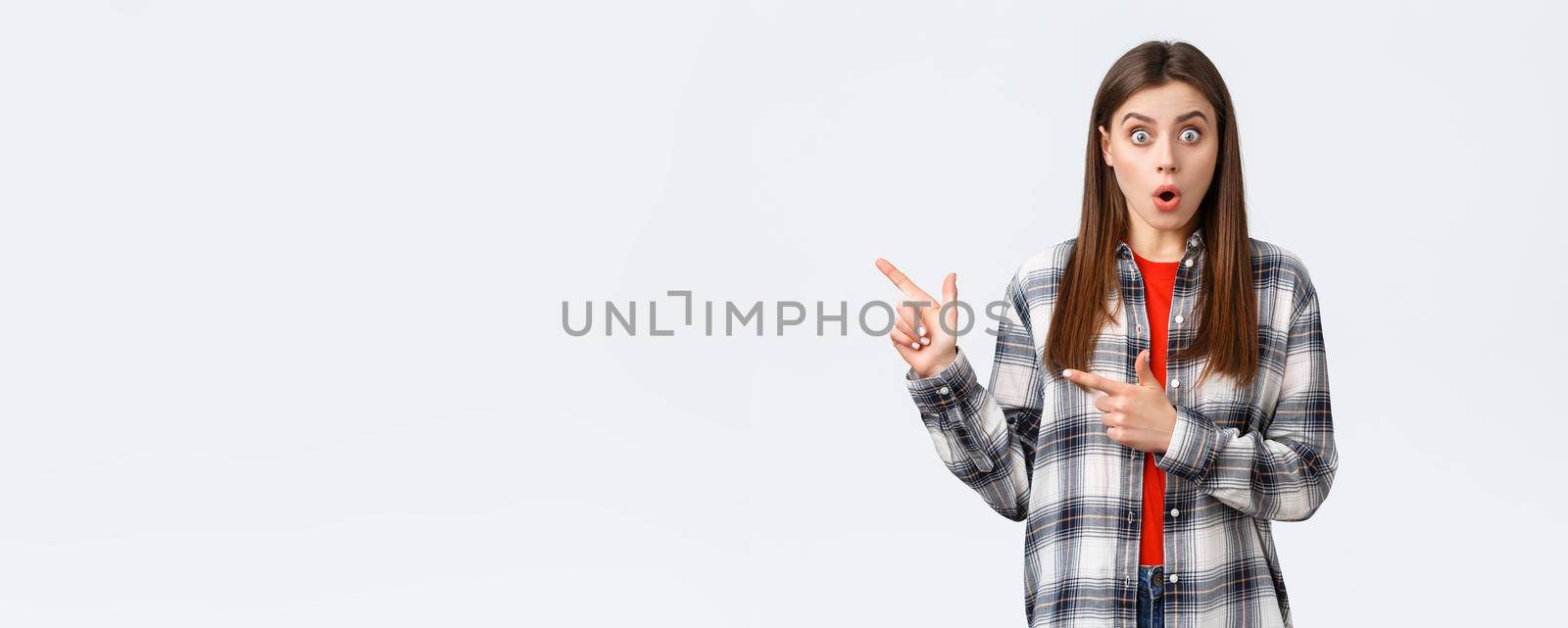 Lifestyle, different emotions, leisure activities concept. Impressed female customer, girl in casual checked shirt, say wow talking about news and pointing fingers left, white background.