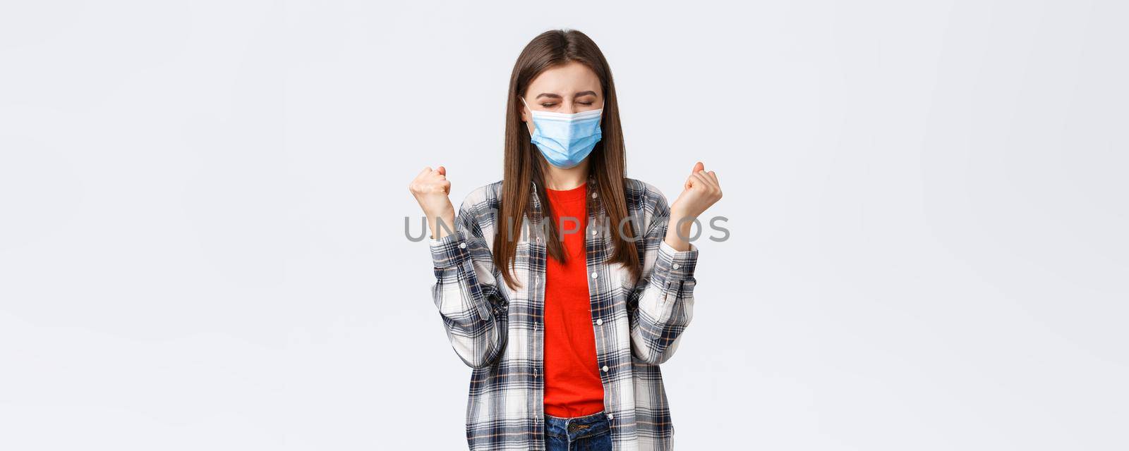 Different emotions, covid-19 pandemic, coronavirus self-quarantine and social distancing concept. Satisfied happy young woman in medical mask, fist pump in celebration victory, success achieved by Benzoix